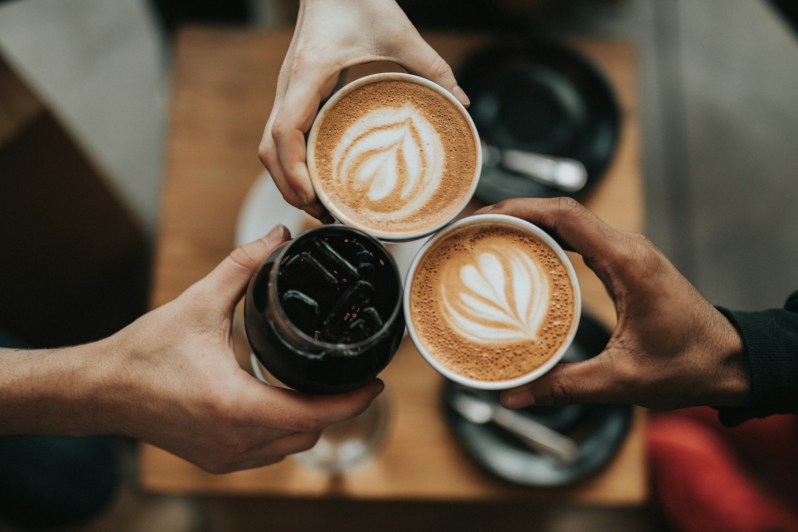 Hands raising coffee cups across a timber table in warm morning light